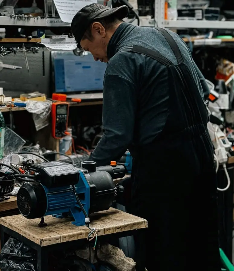 Technician inspecting and repairing a blue water pump motor on a workbench